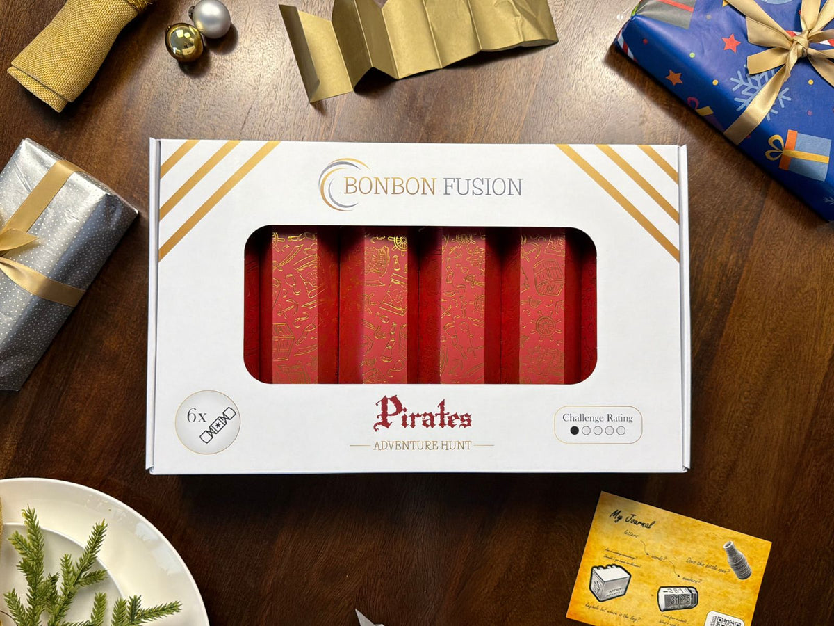 Bonbon Fusion Pirates Adventure Hunt pack of six red and gold foil Christmas bonbons on a festive dinner table, with a gold paper crown, wrapped presents and a "My Journal" puzzle clue card